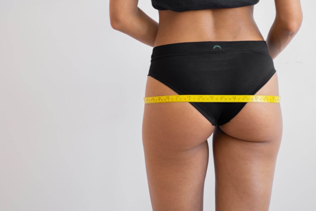 woman measuring the size of her hips while wearing undergarments