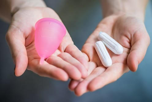 woman holding a pink menstrual cup in one palm and 2 small tampons in the other palm