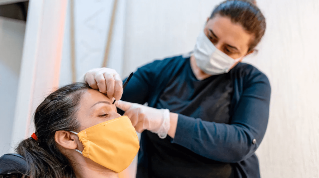 women applying eyebrow makeup to another woman