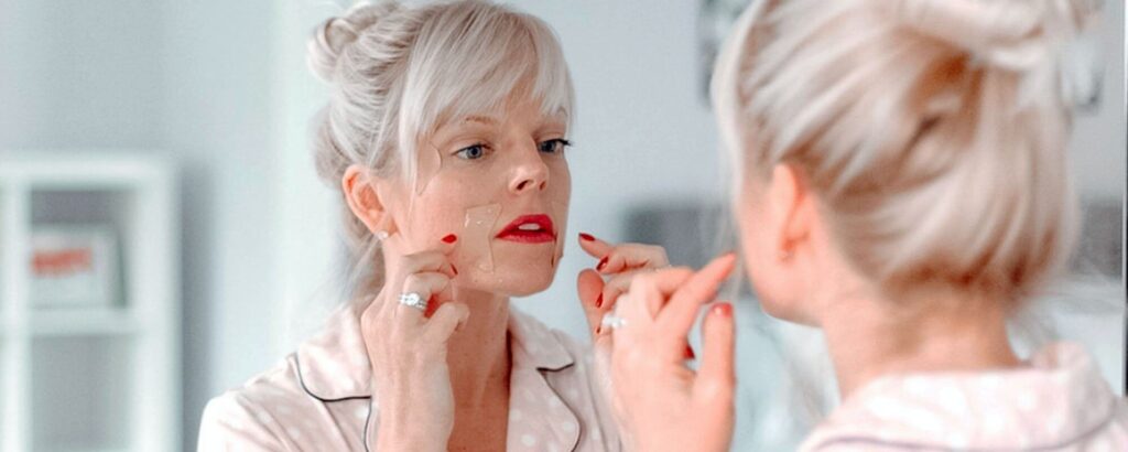 woman with blond hair looking in a mirror and applying frownies