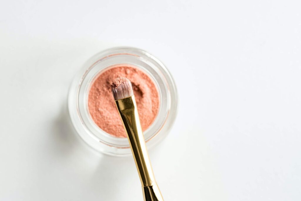 Overhead shot of pink eyeshadow makeup pot and an eyeshadow brush