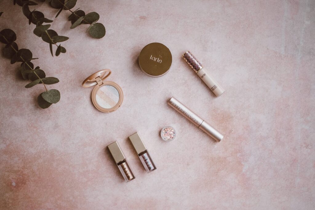 Flat lay of eyeshadow, mascara, lipgloss makeup products on a pink background