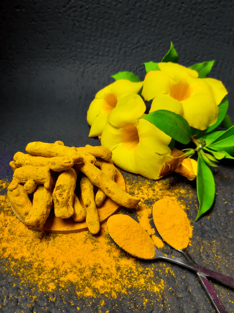 turmeric root and powder with yellow flowers in the background