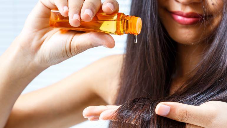 woman with brown hair adding a drop of oil to her dry ends