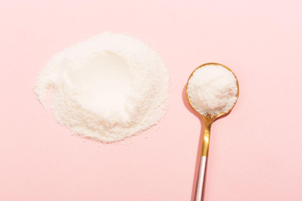 flat lay of white powder and a gold spoon on a pink background