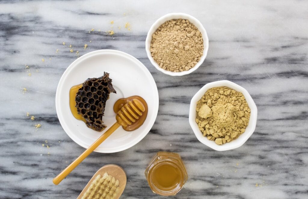 flat lay of honey dipper, honey, honeycomb, brush and powder