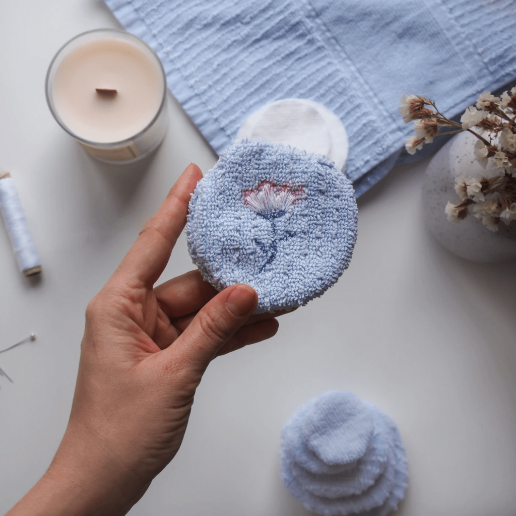 hand showing a blue cotton round with an embroidered flower design