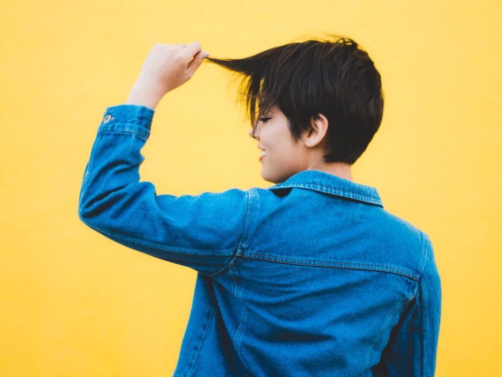 a shorthaired woman facing sideways holding her hair