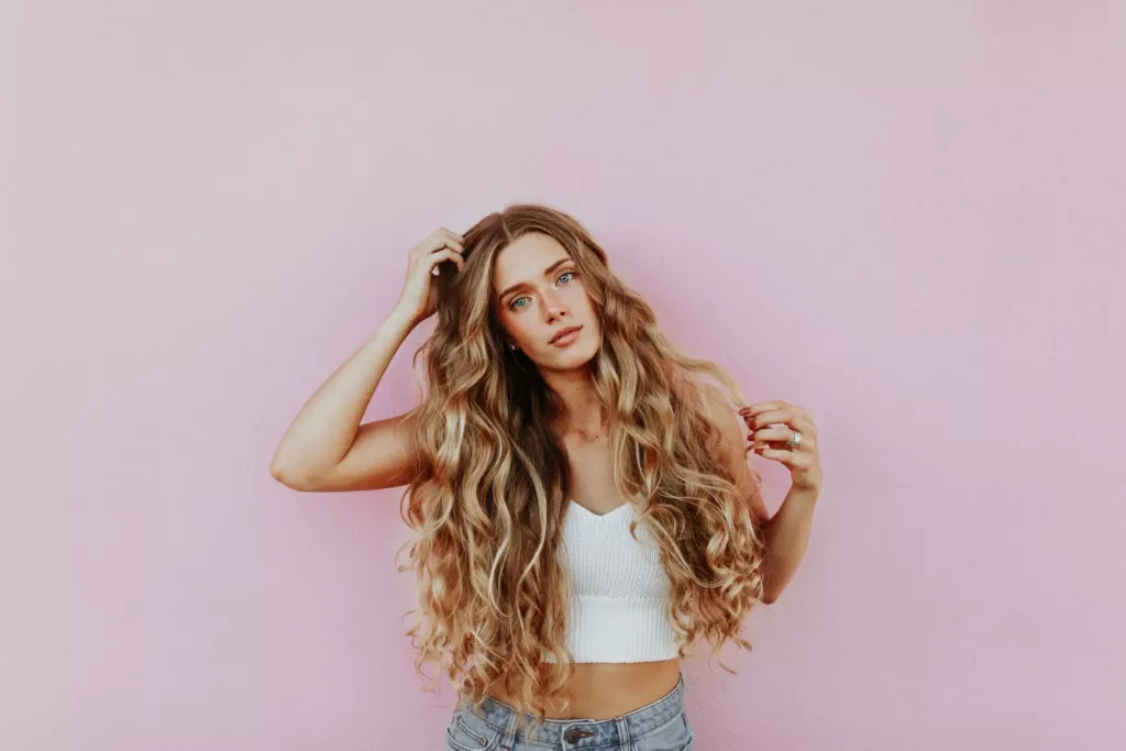 a young woman touching her long, blonde, curly hair