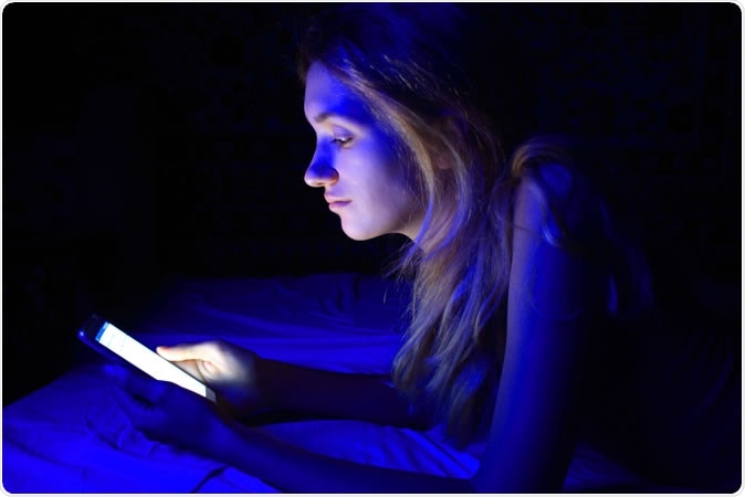 a young woman holding a phone in the dark emitting Blue Light Skin Damage